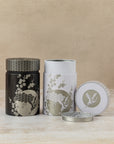 150g pair of cylindrical tea caddies in embossed black, white and gold Japanese design, by The Tea House