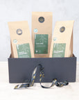Three 100g packs of organic green tea in a black gift box with black and gold ribbon