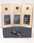 Three 100g packs of organic black tea on a black gift box with black and gold ribbon