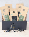 Three 100g packs of organic black tea and two 100g packs of organic green tea in a black gift box with black and gold ribbon