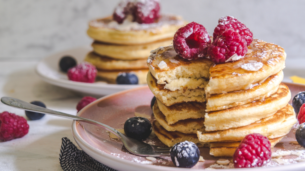 Stacks of fluffy earl grey pancakes on pink plates with raspberries and blueberries.