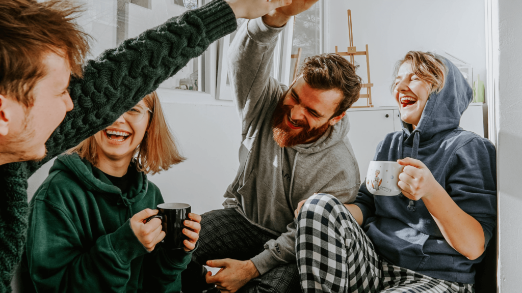 Group of people laughing over a pot of tea.