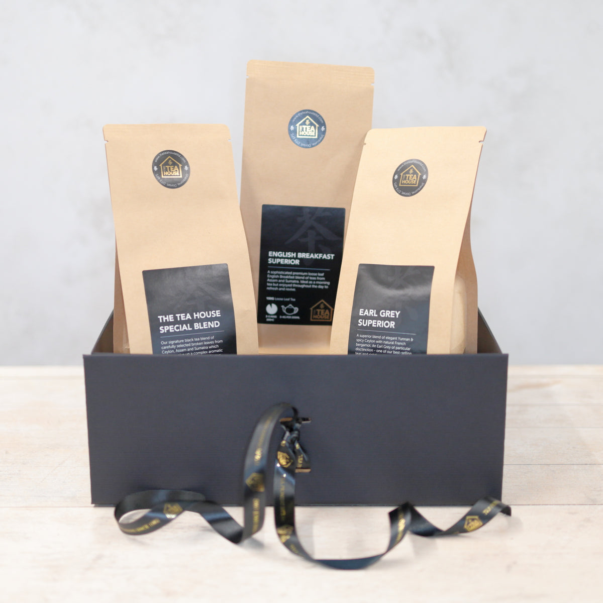 Three 100g packs of black tea in a black gift box with black and gold ribbon