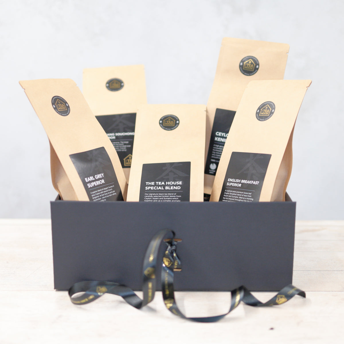 Five packs of black tea in a black gift box with black and gold ribbon