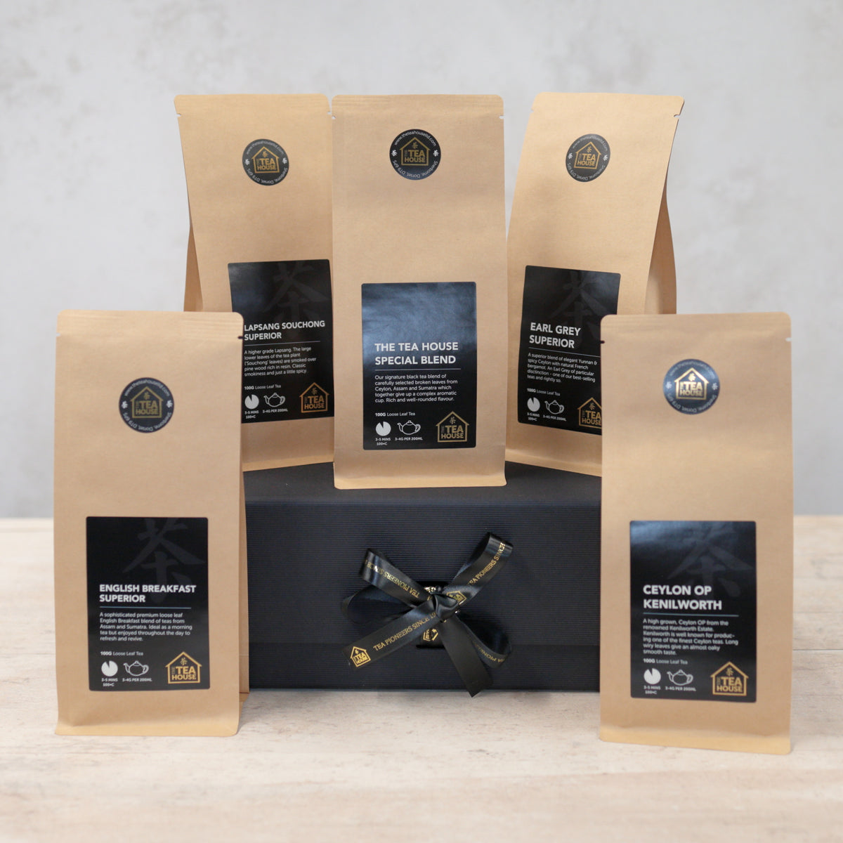 Five packs of black tea on a black gift box with black and gold ribbon
