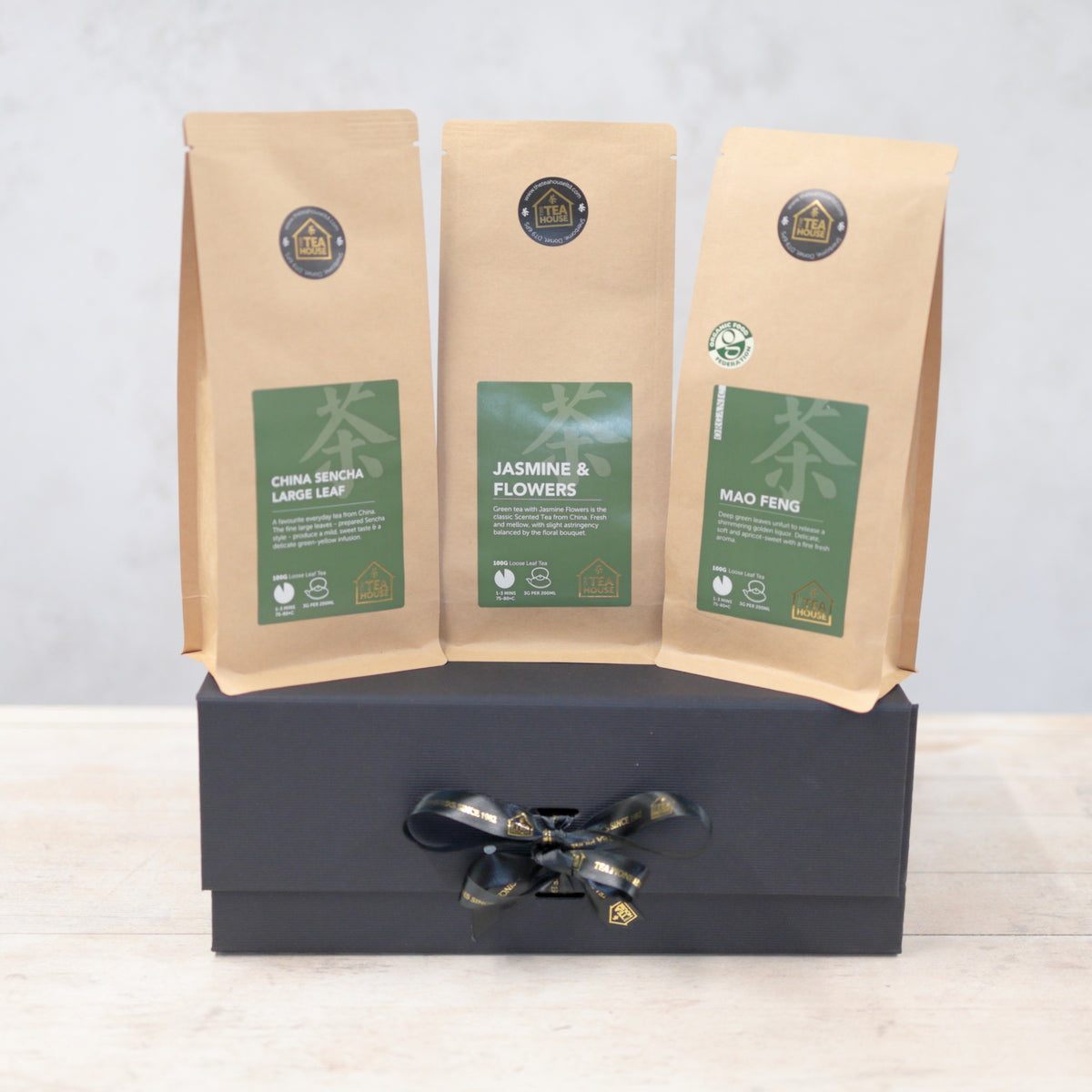 Three packs of green tea on a black gift box with black and gold ribbon