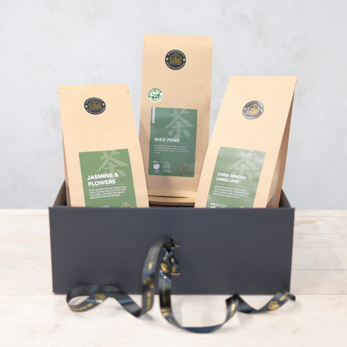 Three packs of green tea in a black gift box with black and gold ribbon