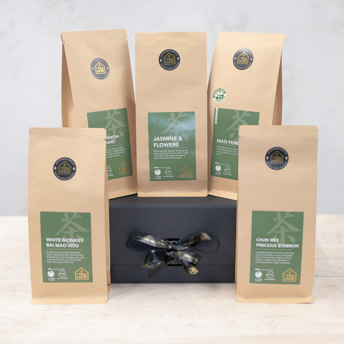 Five packs of green tea on a black gift box with a black and gold ribbon