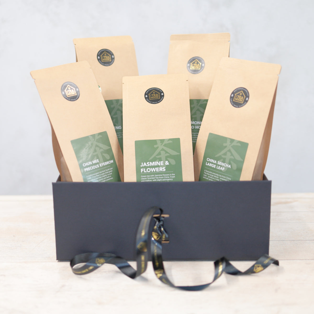 Five packs of green tea in a black gift box with a black and gold ribbon