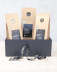 Three 100g packs of organic black tea in a black gift box with black and gold ribbon