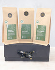 Three 100g packs of organic green tea on a black gift box with black and gold ribbon