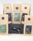 Three 100g packs of organic black tea and two 100g packs of organic green tea on a black gift box with black and gold ribbon  